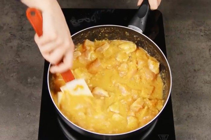 Hand stirring korma in a pan