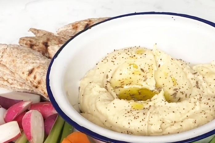 Hummus in a bowl surrounded by vegetables and pitta bread