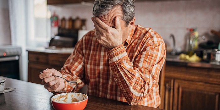 An older man holding his head whilst eating