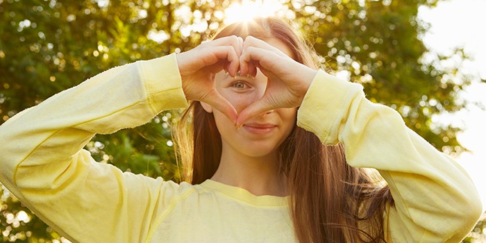 A woman making a heart shape with her hands over her eye