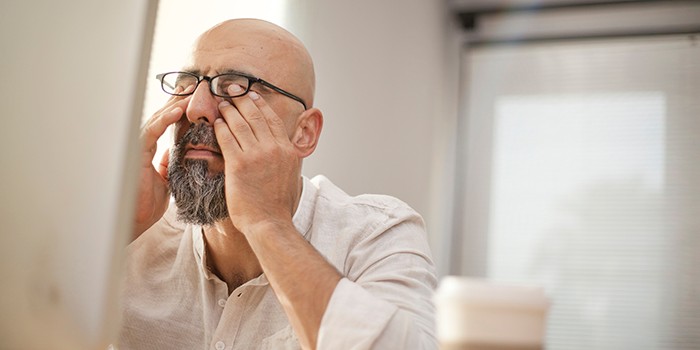 Tired man rubbing his eyes as he sits at his computer, cup of coffee close by