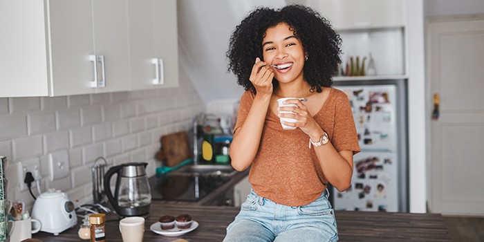 Woman eating a tub of yogurt in the kitchen
