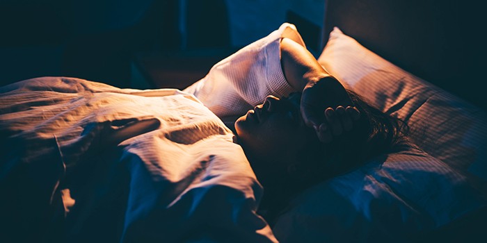 Young woman lying on bed with hand on forehead.