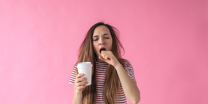 Woman yawning, holding a cup of coffee