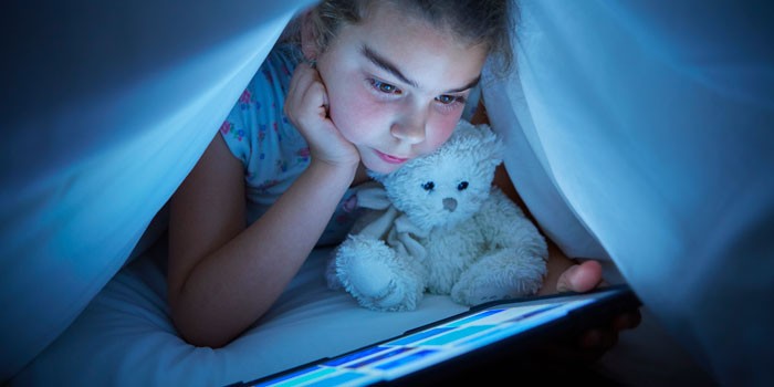 A child looking at a tablet under duvet covers