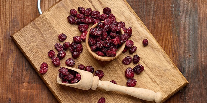 Wooden bowl of dried cranberries on a wooden chopping board with a wooden ladle of cranberries beside it