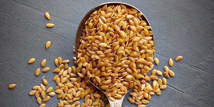 A spoon of flaxseeds, with some spilling on to the counter top beneath