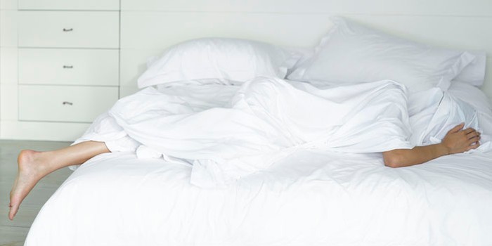 Person hiding under white bed covers