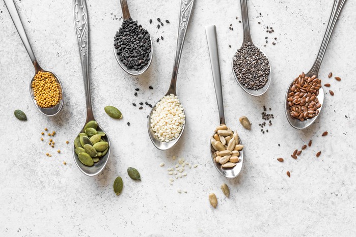Spoons with various different seeds lying on a white background