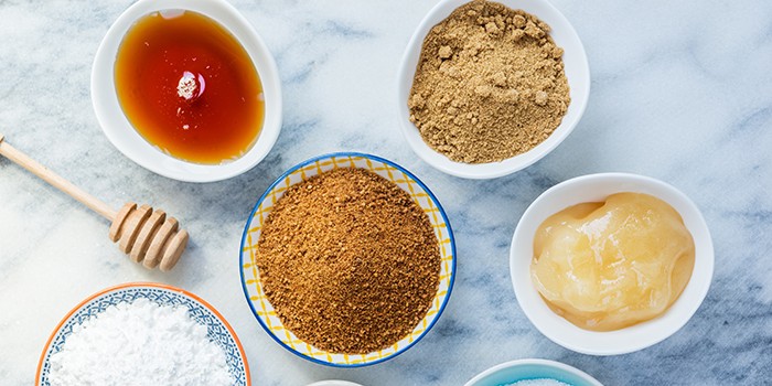 Different Kinds of Sugar and Sweeteners in the Bowls, such as coconut, pure cane, icing, maple syrup, dark brown soft sugar, honey, demerara cubes