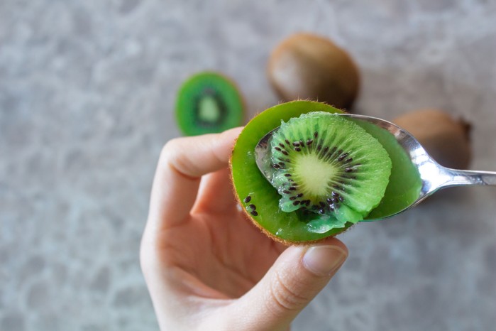 Hands spooning out the innards of a kiwi