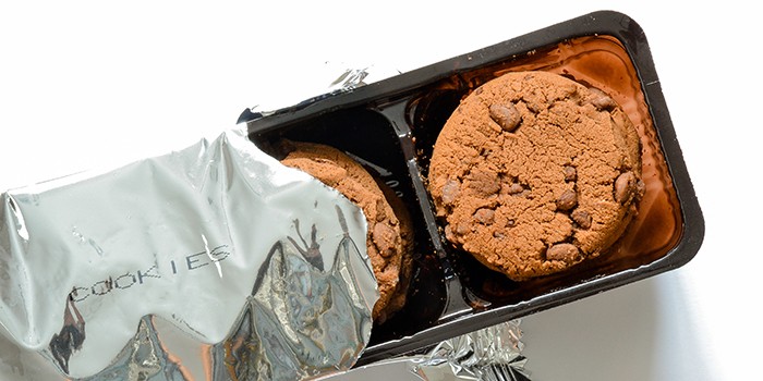 Packet of industrially-produced cookies, with the silver foil packet torn back to reveal the chocolate-chip cookies inside
