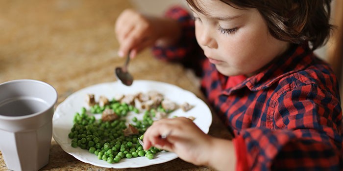 A young child eating peas
