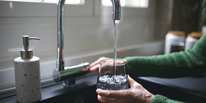 A person holding a glass under a running tap