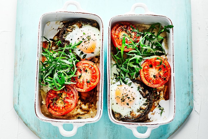 Two dishes with tomatoes, mushrooms and eggs topped with rocket