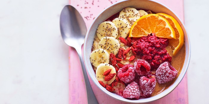 Bowl of porridge topped with frozen berries, sliced fruit and peanut butter