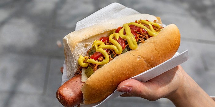 Hotdog with sauces, pickles and fried onions in a white bread roll