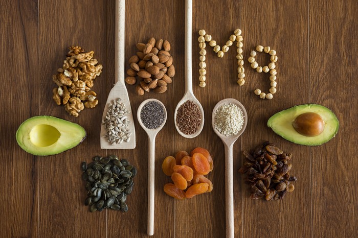 Foods that contain magnesium in small piles and on spoons and the chemical symbol for magnesium