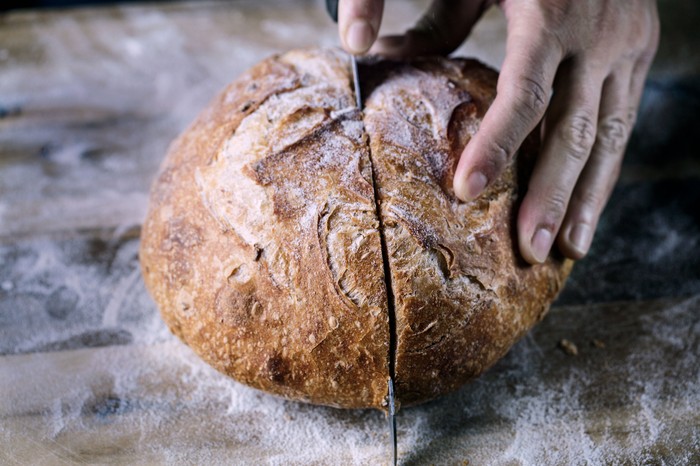 Hands cutting sourdough loaf in half