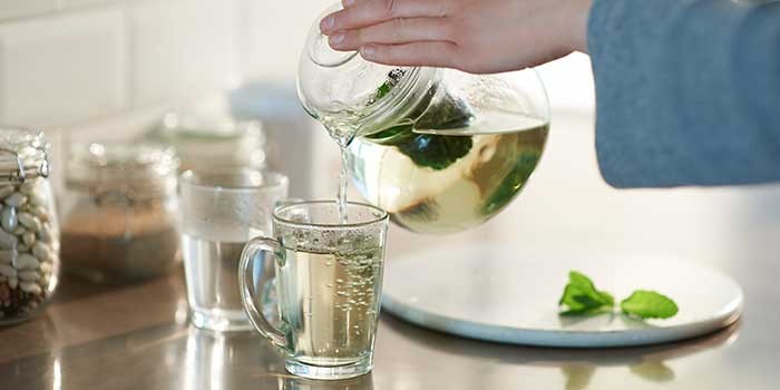 Someone pouring a mint tea from a glass teapot