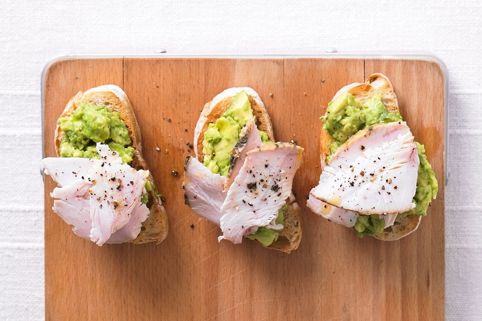Three slices of avocado toast topped with turkey slices