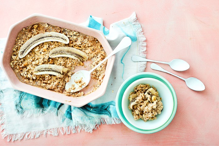 Baking dish of oats with whole bananas. In a bowl is a serving