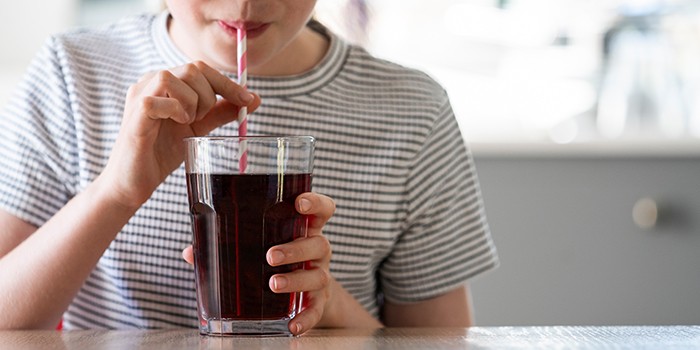 Child drinking glass of cola with a straw