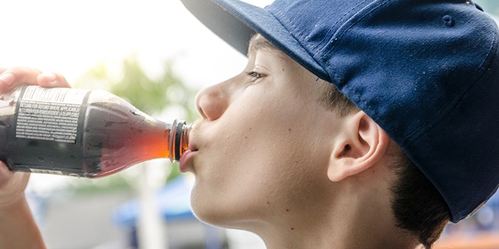 Boy in baseball cap drinking from a bottle of cola, profile