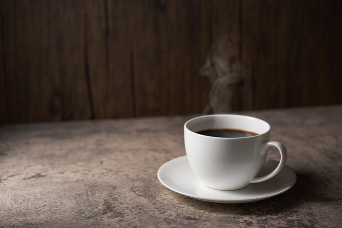 Steaming white cup of black coffee, on a wooden table
