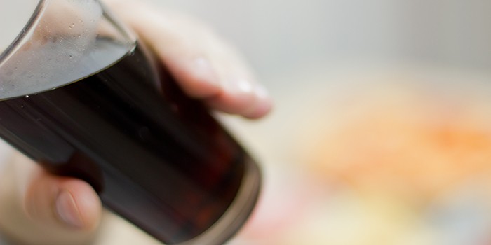 A child's hand holding a glass of cola