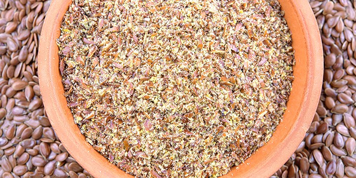 Dish of ground flaxseed against a background of whole flaxseeds
