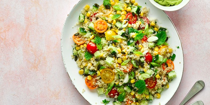 Quinoa salad with avocado mayo on a white plate with a pink background