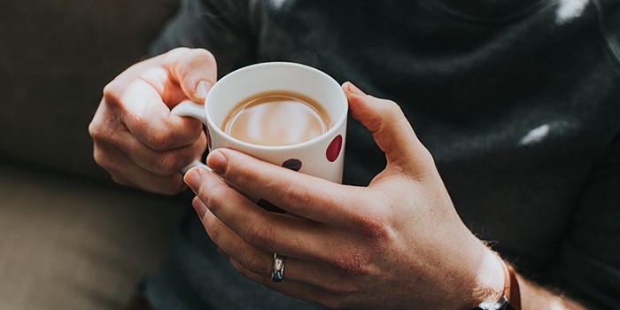 Hands holding a white and spotty mug of tea