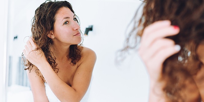 Woman in a towel looking in mirror and applying hair treatment