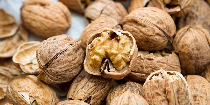 A pile of whole walnuts with one opened, showing the nut within the shell