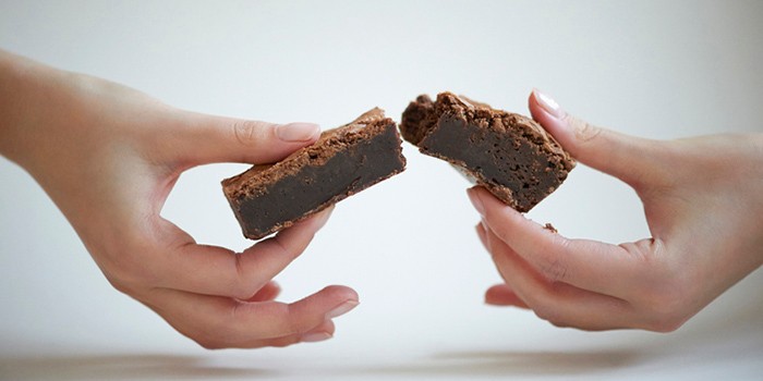Close up of female hands breaking a home made chocolate brownie in half against a white background.