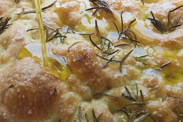 Baked focaccia being topped with olive oil